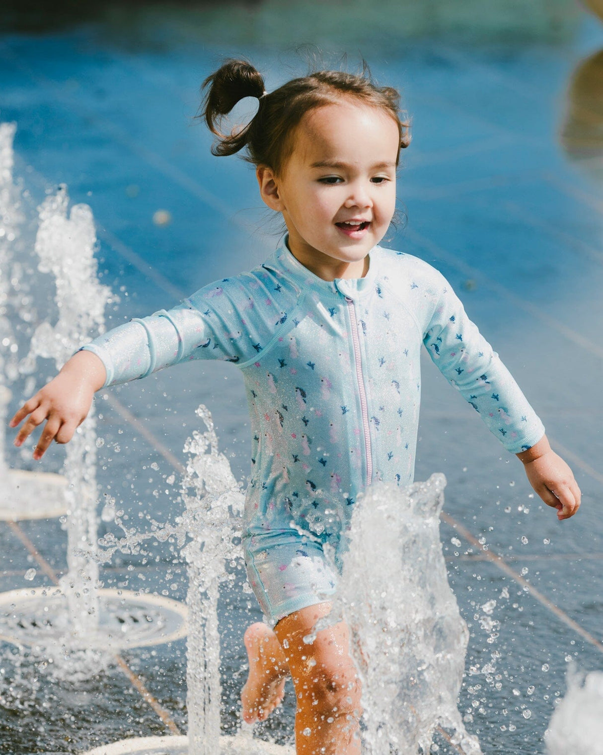 Baby girl playing by the water wearing blue seahorse rashguard one-piece