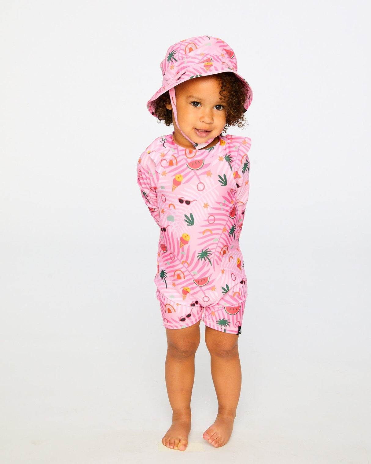 Little girl standing in pink beach print rashguard suit and matching sun hat