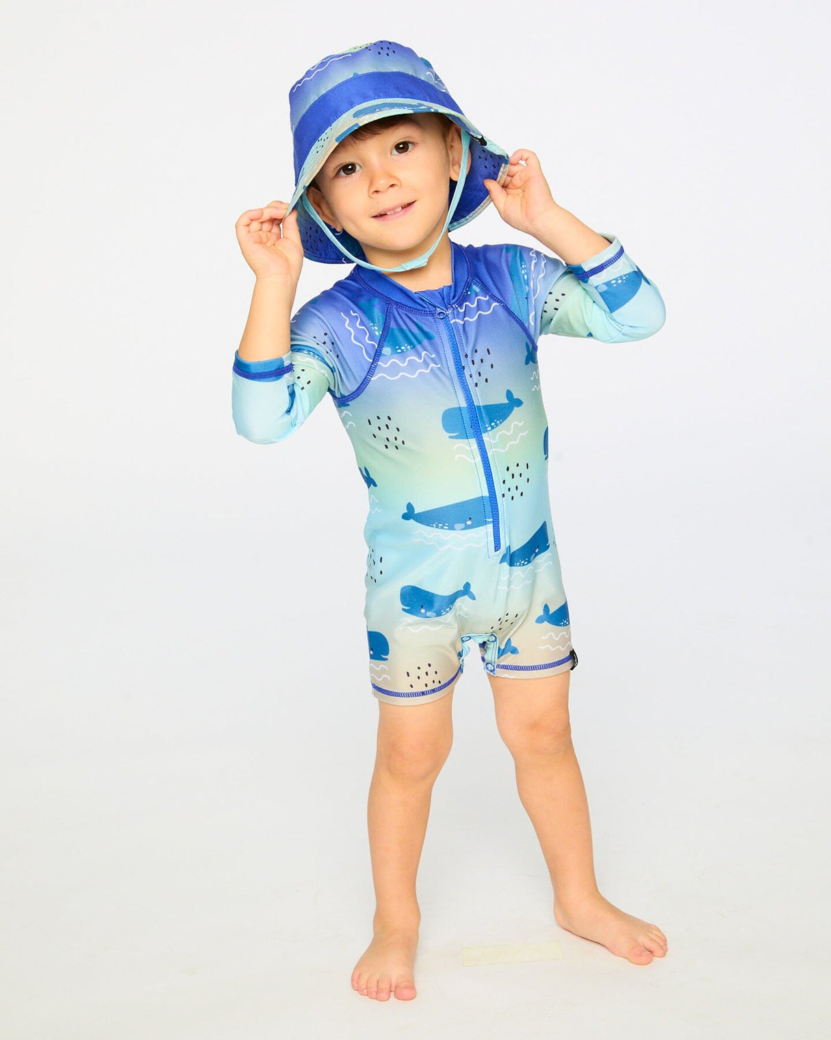 Toddler boy standing in blue whale long sleeve rashguard swimsuit front view
