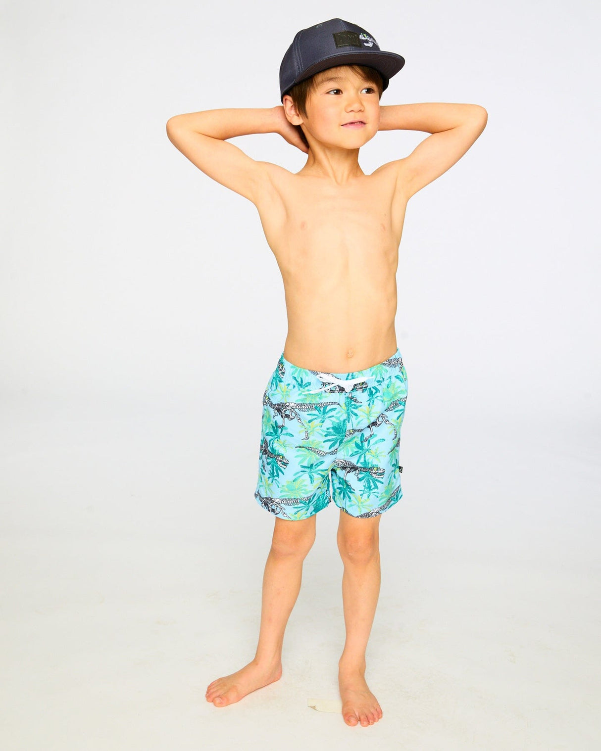 Boy standing with hands behind head showing front view of blue skeleton boardshorts