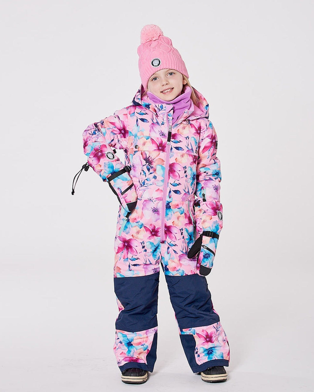 Girl wearing the pink watercolor flower one-piece Teknik snowsuit — front view on snow