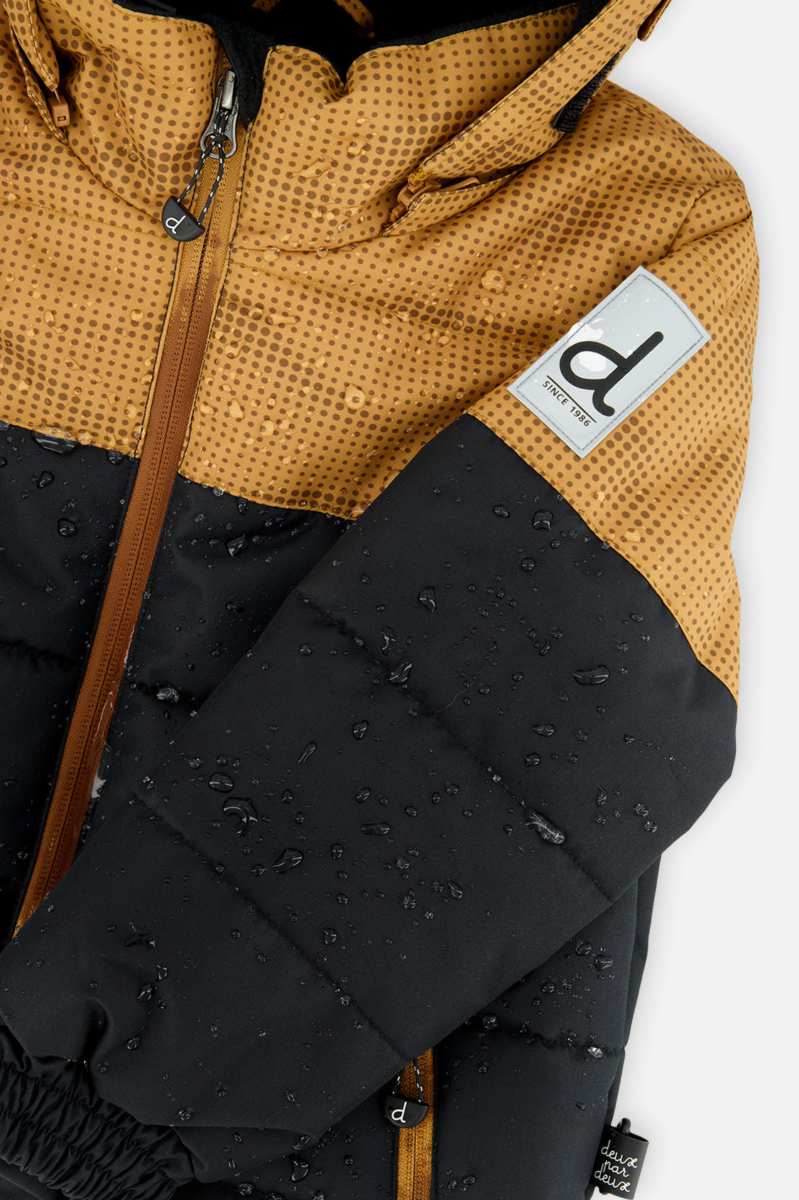 Deux par Deux boys PLAY snowsuit, brown and black – close-up of the water-repellent jacket shell and logo patch