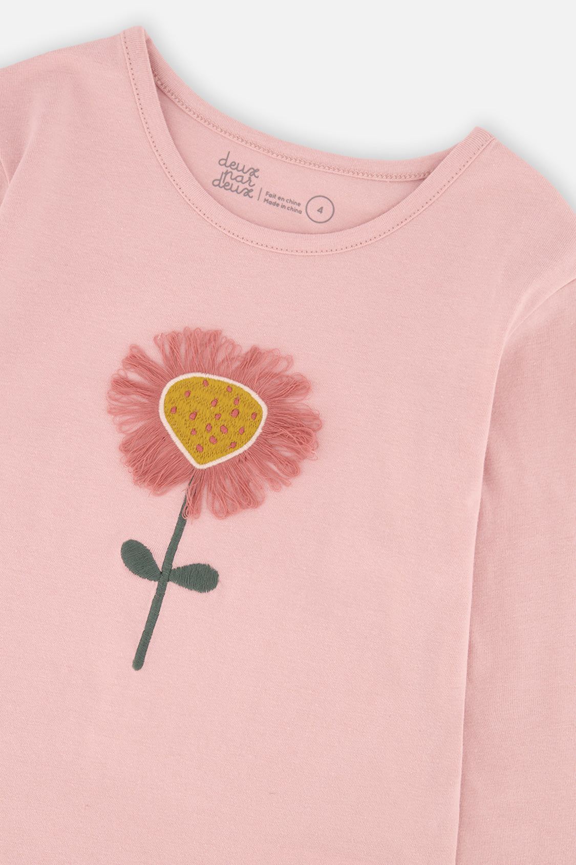 Close-up of the 3D embroidered pink flower with a mustard center on the tee