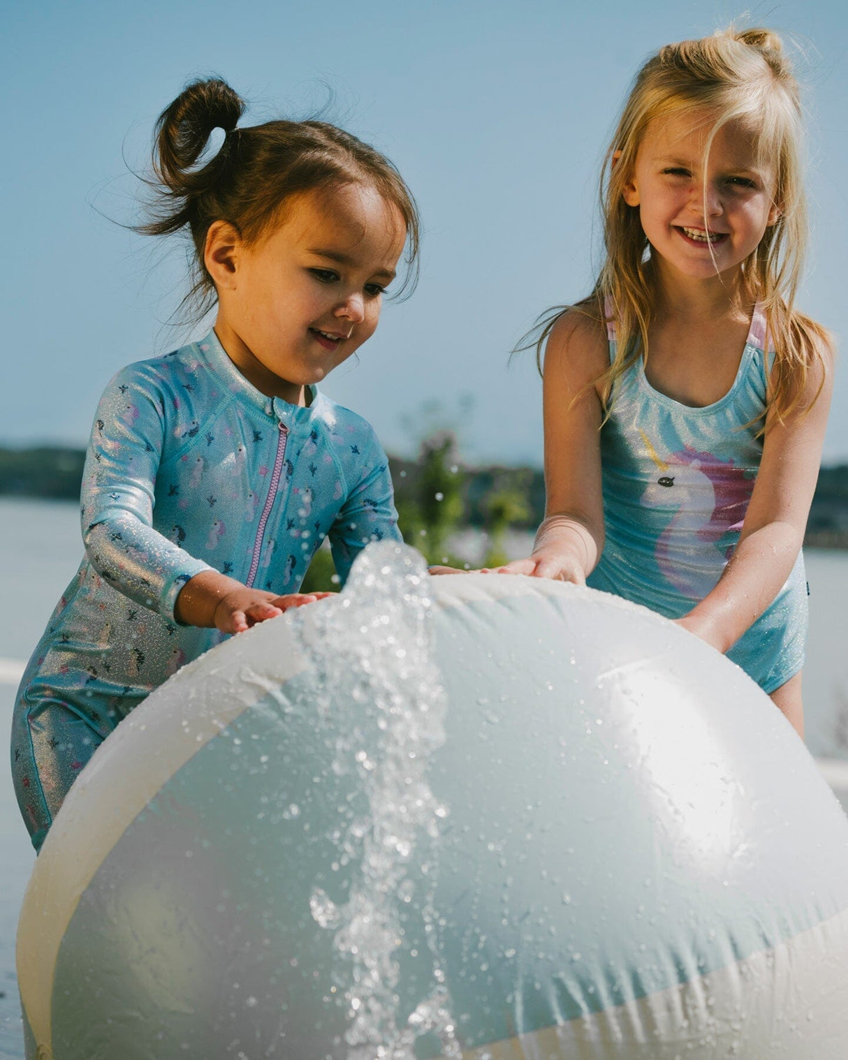 Two girls playing with beach ball, one in aqua seahorse kids swimsuit