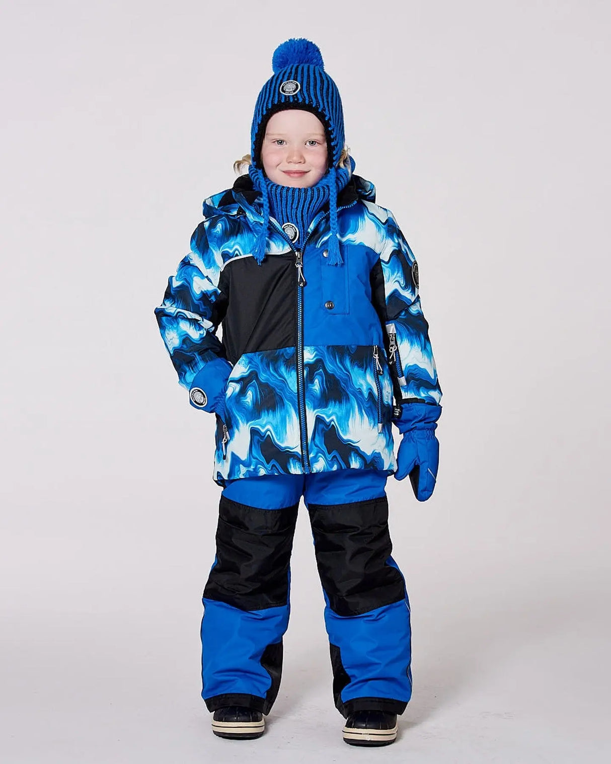 Boy wearing blue jacket and snow pants with detachable hood and snow skirt.