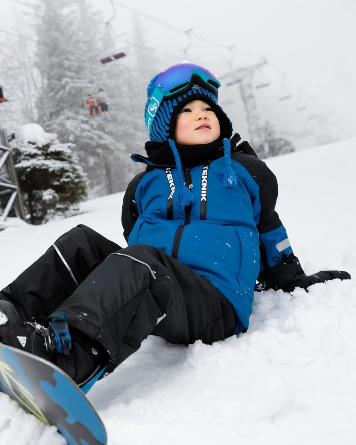 Action shot: boy in blue jacket and snow pants, helmet-friendly hood.