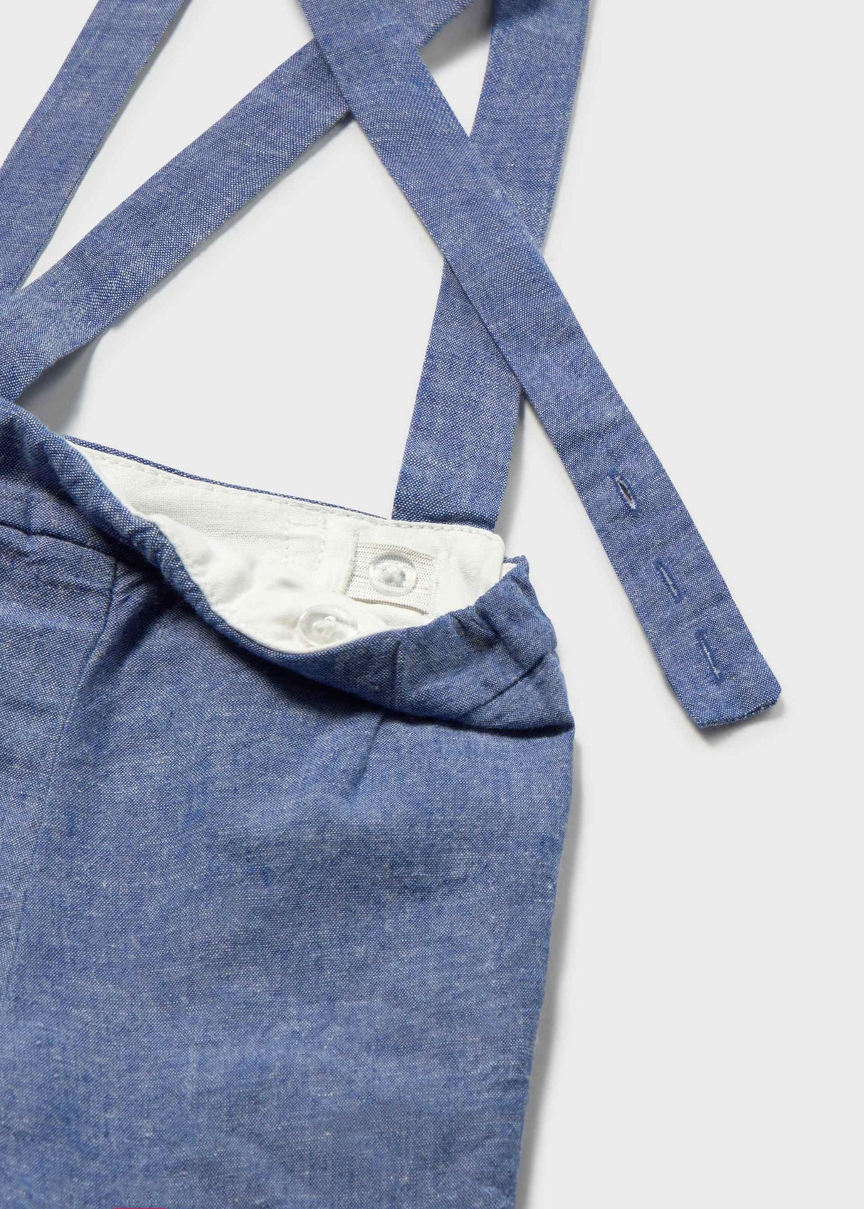 Closeup of blue Bermuda shorts with suspender straps and cotton-linen fabric detail.