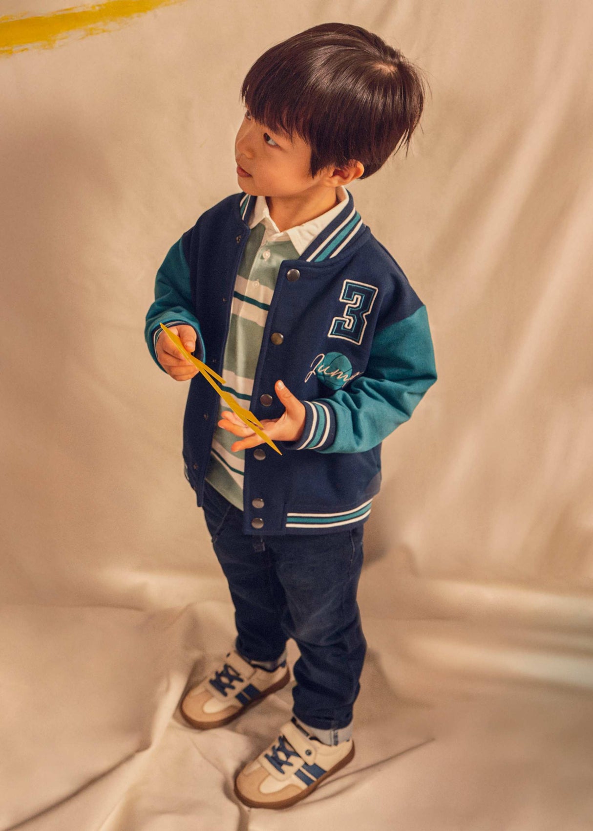 Boy wearing Mayoral dark blue jeans with varsity jacket and sneakers for casual everyday style.