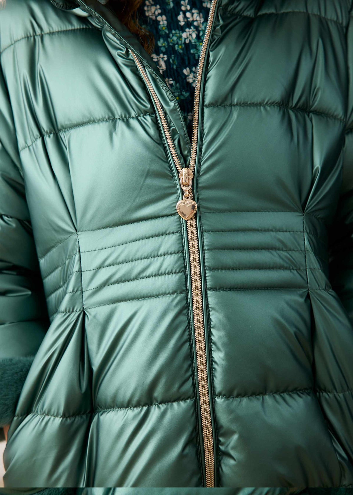 Close-up of the gold zip pull and quilted waist on the metallic green puffer