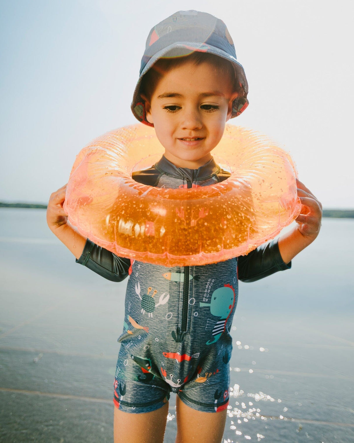 Baby boy playing at the beach wearing blue marine animals rashguard one-piece and sun hat