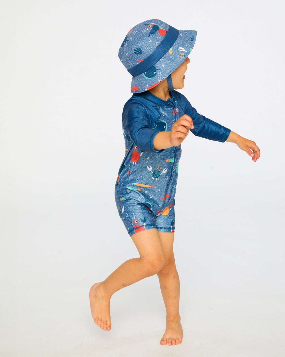 Toddler boy walking in side view wearing blue marine animals long sleeve rashguard swimsuit