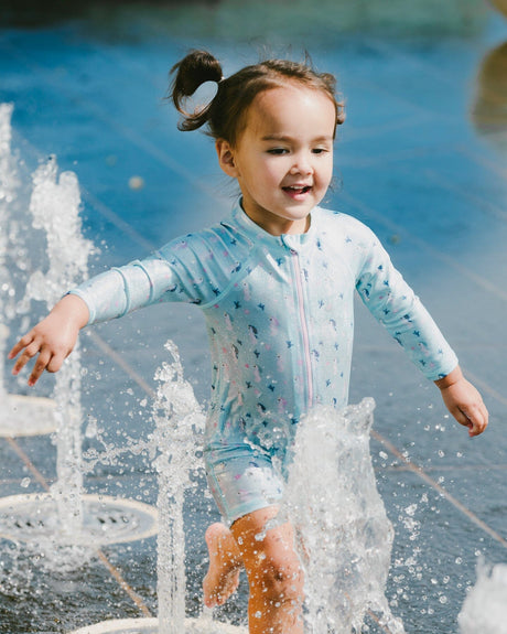 Baby girl playing by the water wearing blue seahorse rashguard one-piece