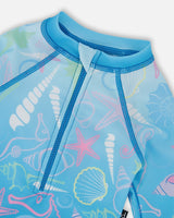 Close-up of neckline, zipper, and pastel shell print on blue girl rashguard swimsuit