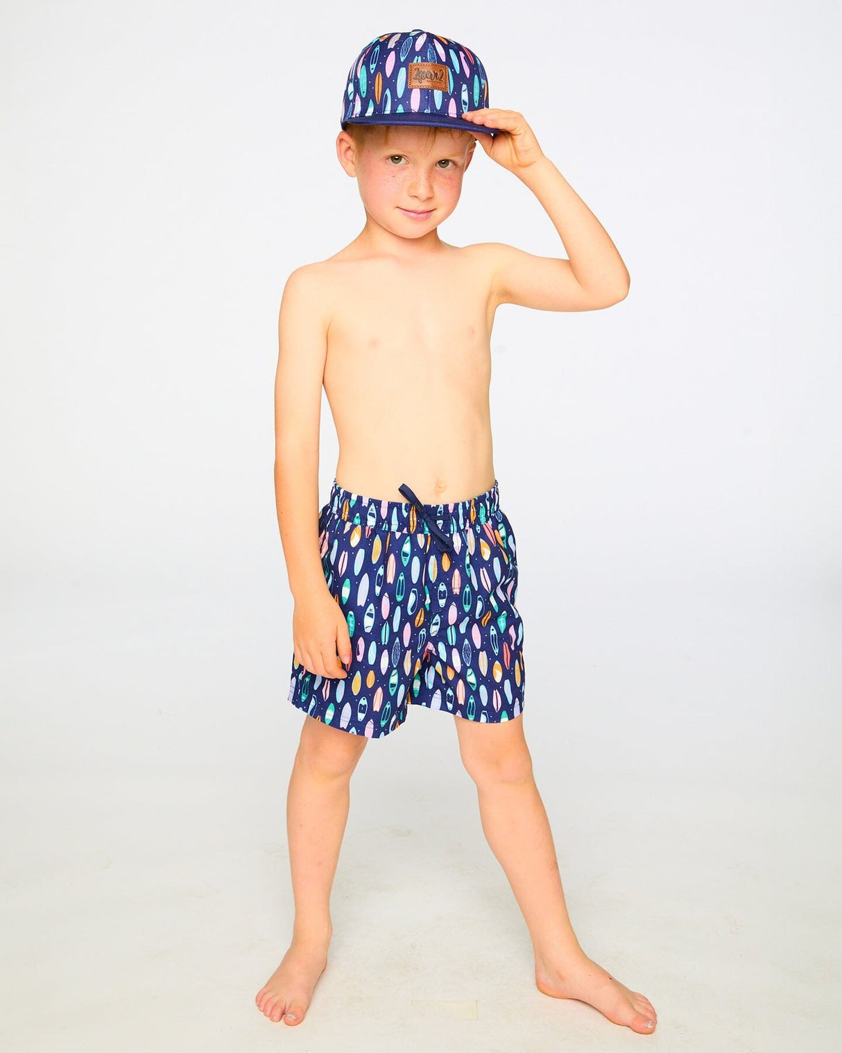 Boy standing in studio in navy surfboard swim shorts above the knee