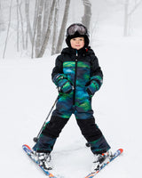 Child wearing Aurora Borealis one-piece Teknik snowsuit – front on snow