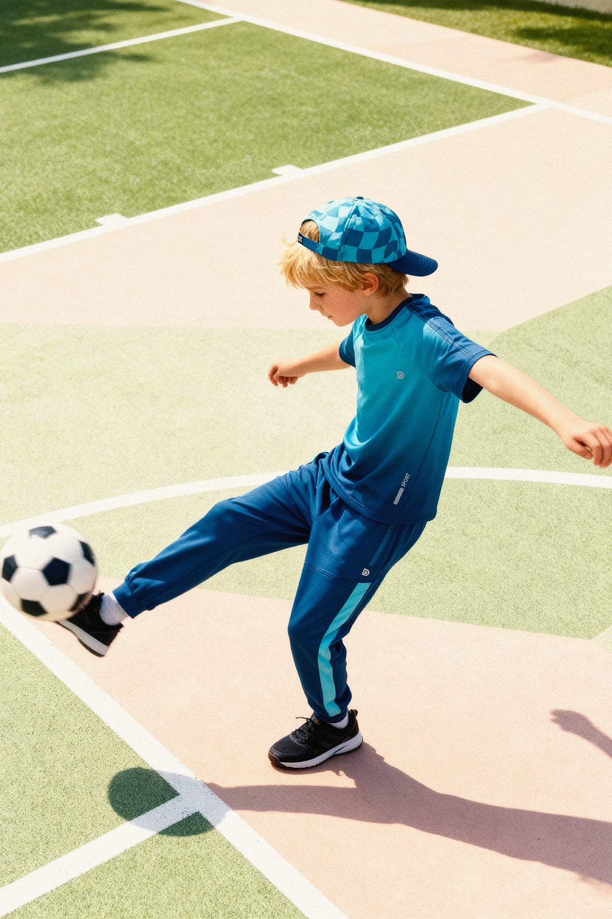 Child kicking a soccer ball in the teal track pants with a matching top and cap