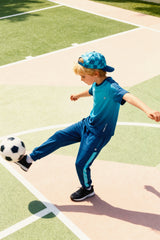 Child kicking a soccer ball in the teal track pants with a matching top and cap