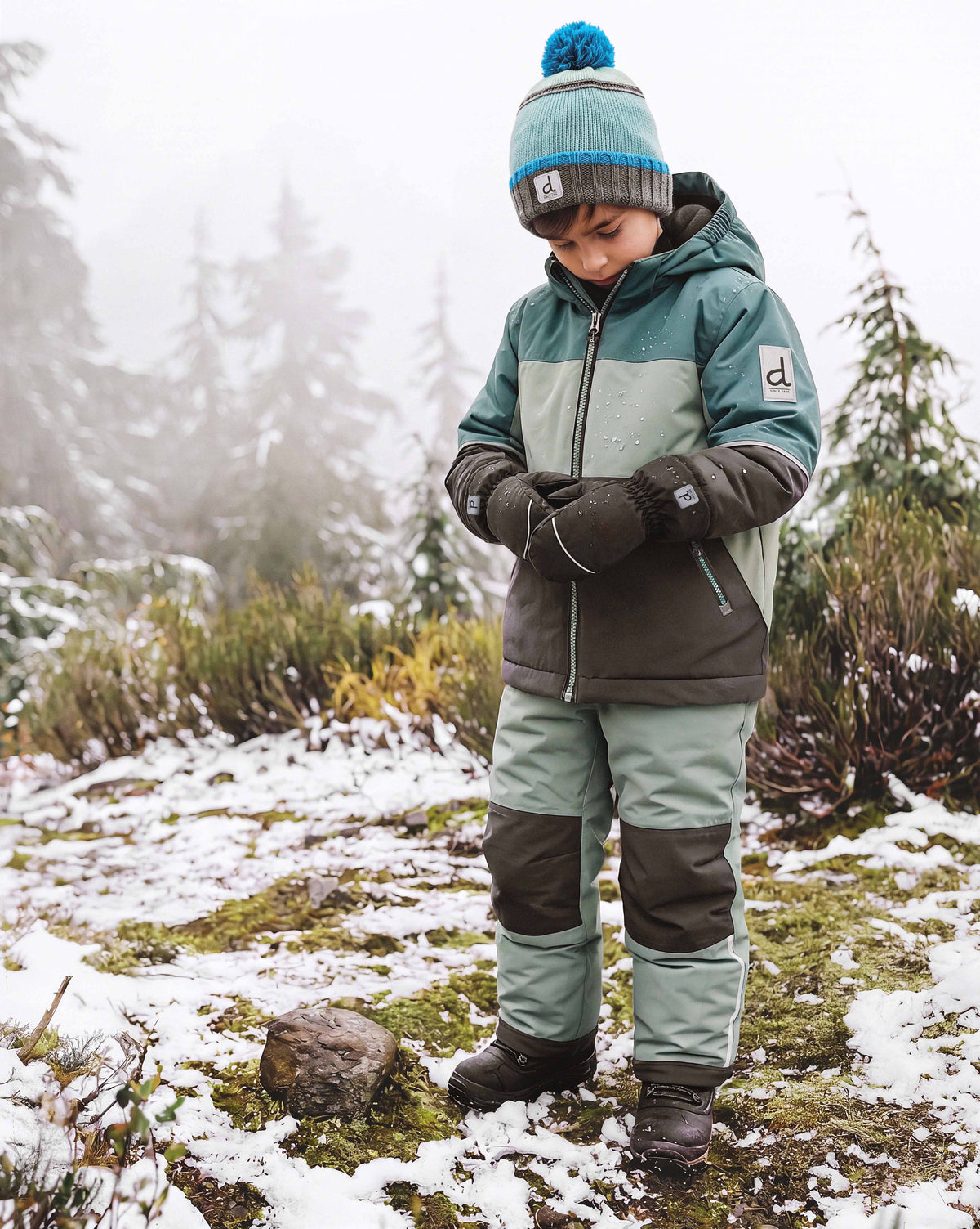Child wearing the Deux par Deux CHILL lightweight snowsuit in Sage Green, lifestyle view