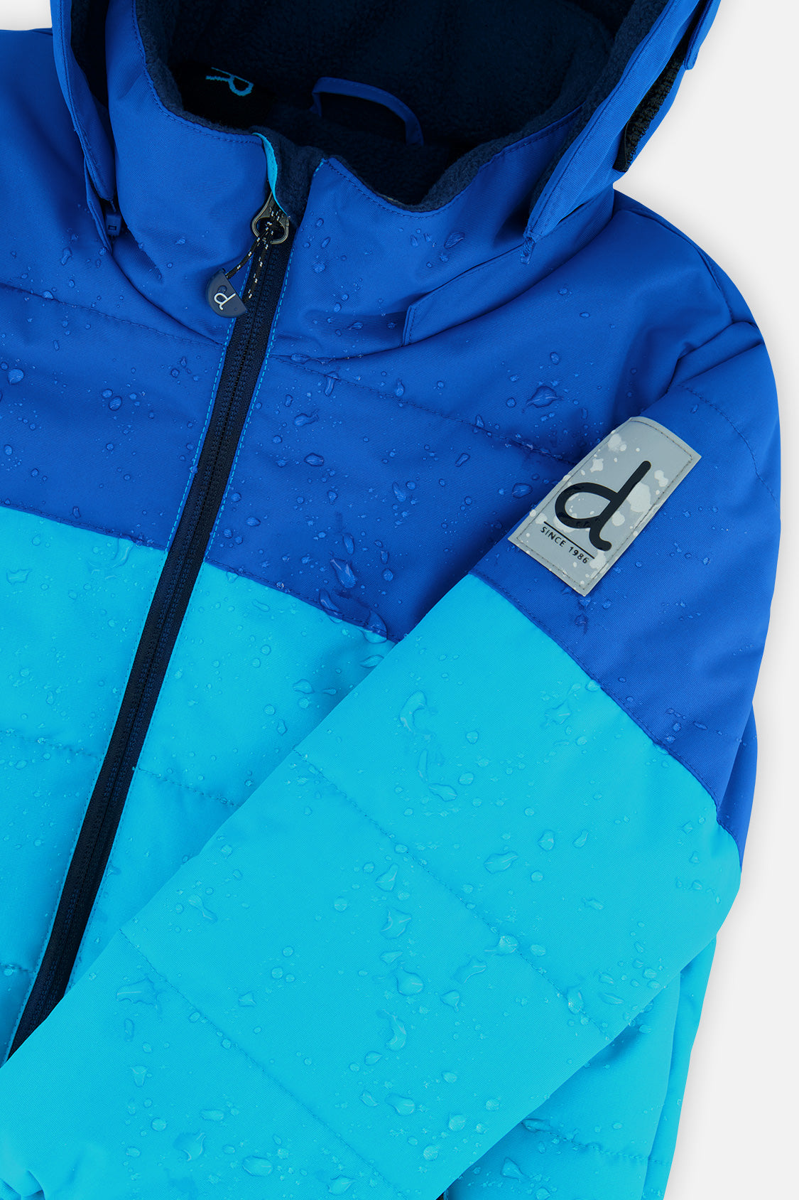 Deux par Deux boys PLAY snowsuit, light and dark blue – close-up of the water-repellent jacket shell and logo patch