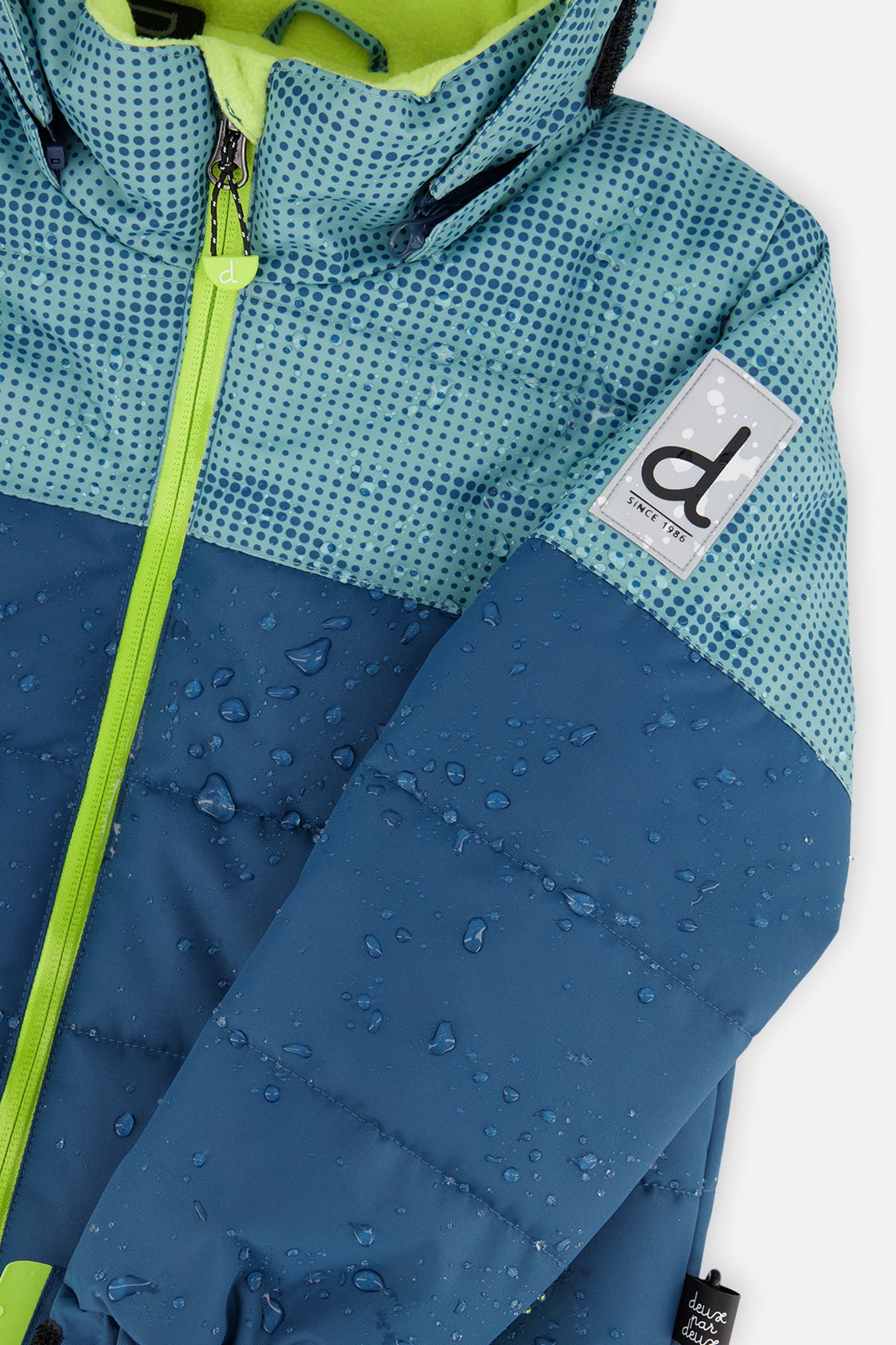 Close-up of the Deux par Deux greyish blue and navy PLAY jacket shell, zipper and logo patch