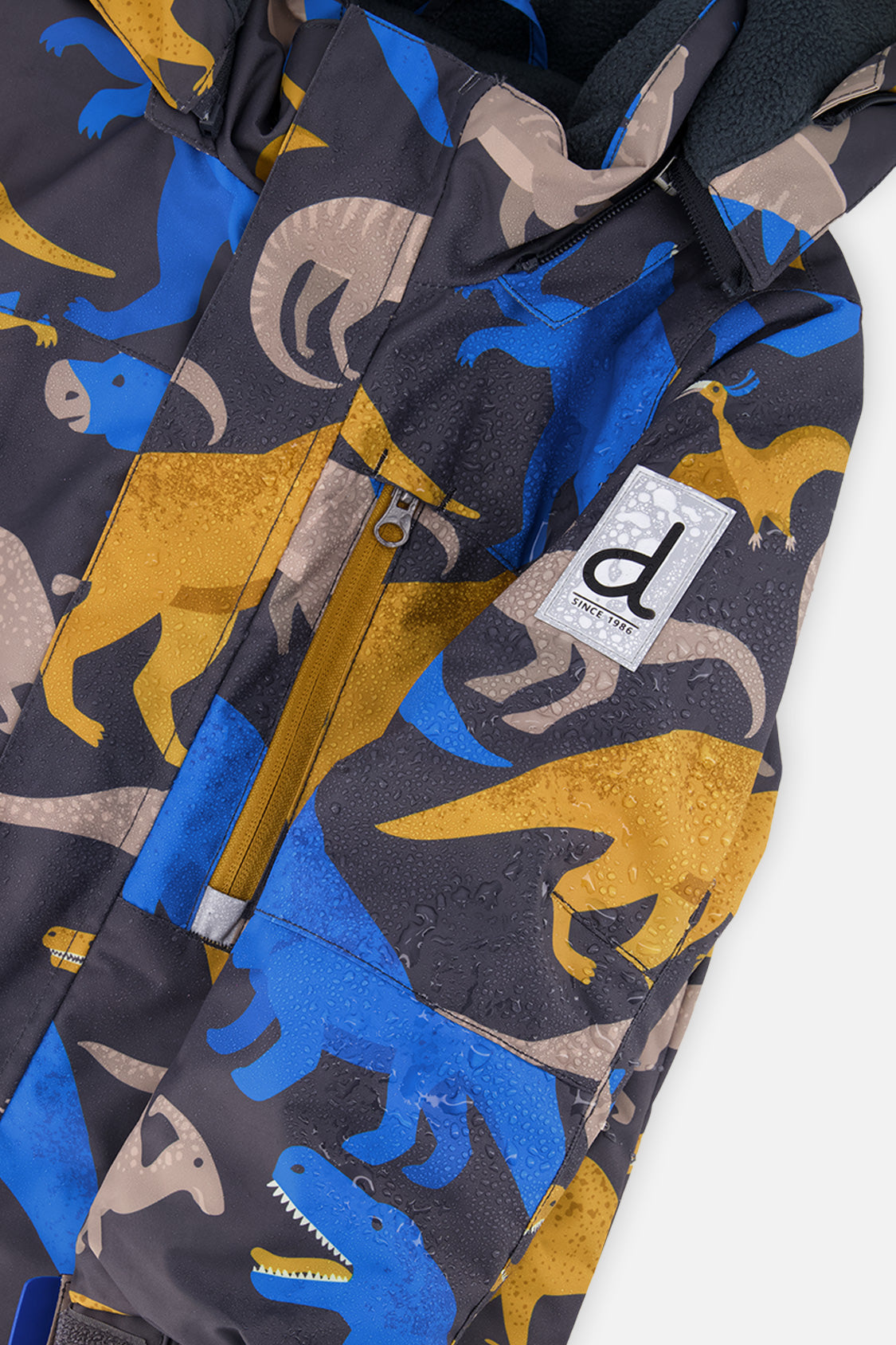 Close-up of the dinosaur-print PLAY jacket front zipper, chest pocket and sleeve logo patch