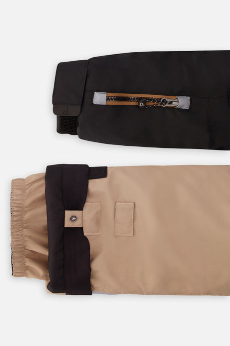 Close-up of the black PLAY jacket sleeve ski-pass pocket and the adjustable beige pant hem