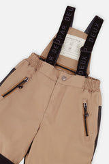 Close-up of the beige PLAY snow pants waist, zip pockets and Deux par Deux logo suspenders