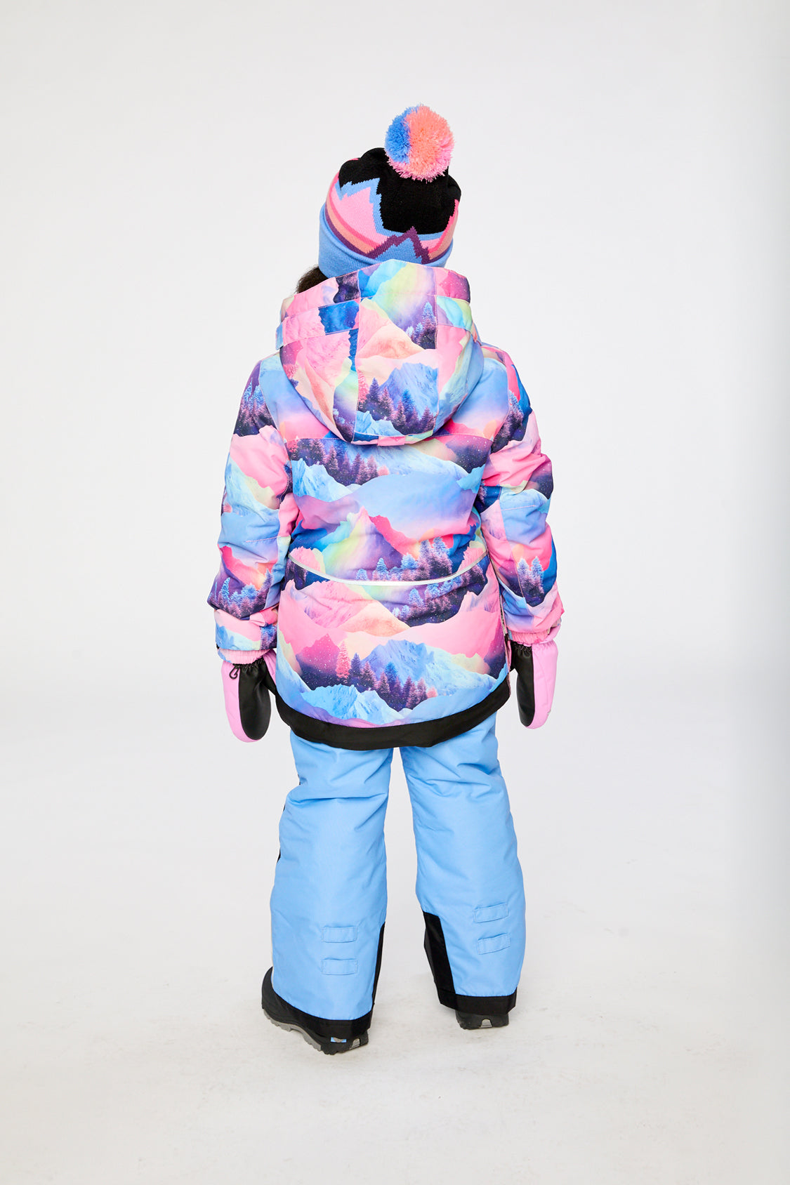Child in the pink mountain-print PLAY snowsuit with blue pants, back view