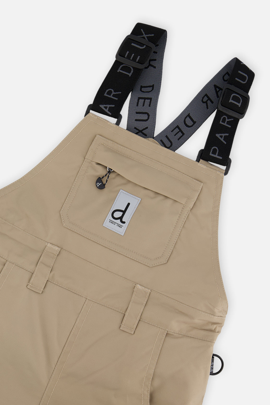 Close-up of the taupe snow bib chest pocket, logo patch and suspenders