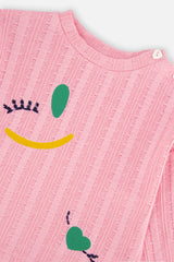 Close-up of the shoulder button, crew neckline and winking face motif on the pink knit top