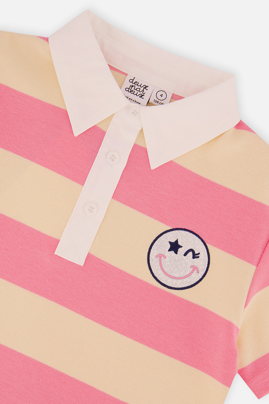 Close-up of the white collar, button placket and smiley badge on the pink and beige striped polo