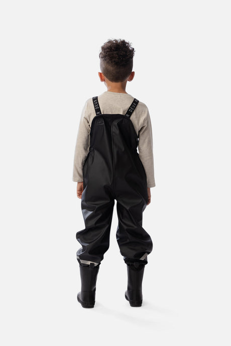 Lifestyle photo of a child wearing the Deux par Deux black waterproof rain overalls