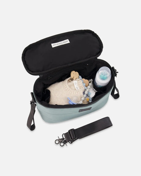 Open sage green bag with a black lining, holding a bottle and folded baby clothes