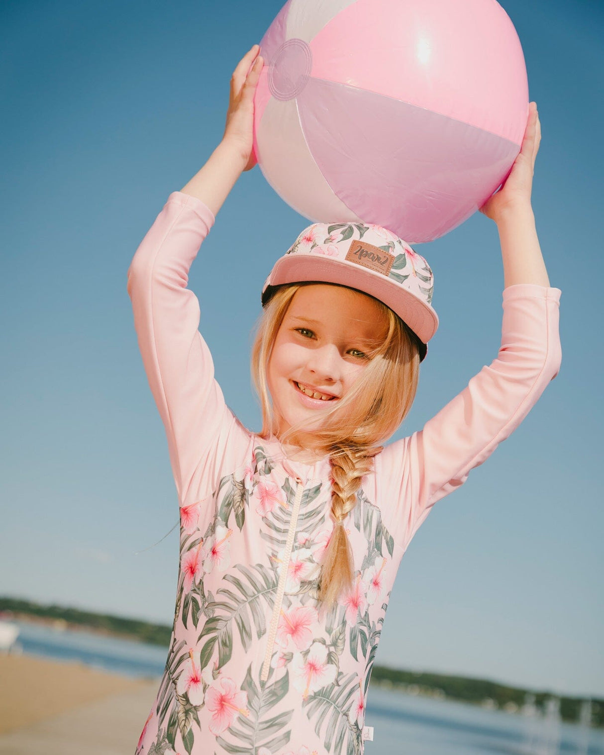 Girl holding a beach ball wearing pink hibiscus one-piece rashguard at the shore