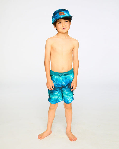 Boy standing in studio wearing blue waves swim shorts above the knee