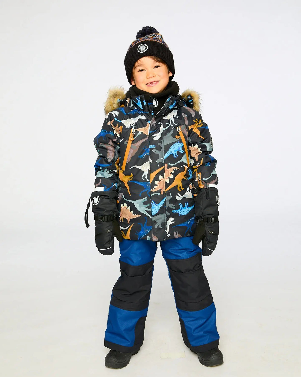 Child wearing Deux Par Deux dinosaur-print jacket with navy bib pants, warm and breathable