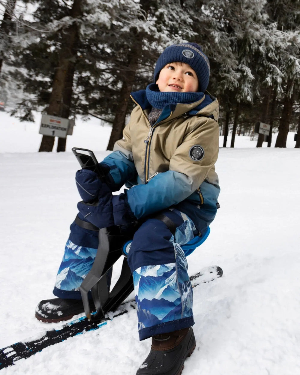 Action shot in blue jacket and snow pants, detachable hood and snow skirt.