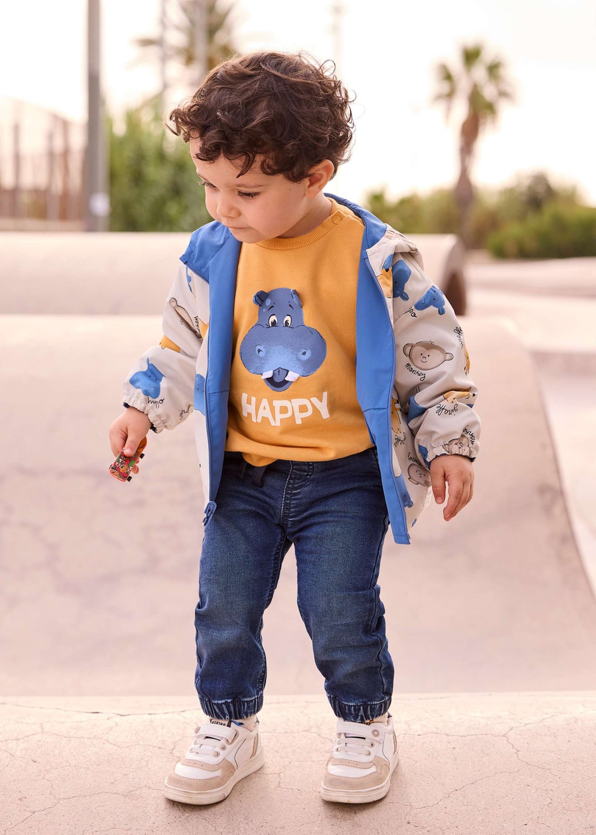 Child wearing Dark Blue Mayoral jogger jeans outdoors with jacket and sneakers.