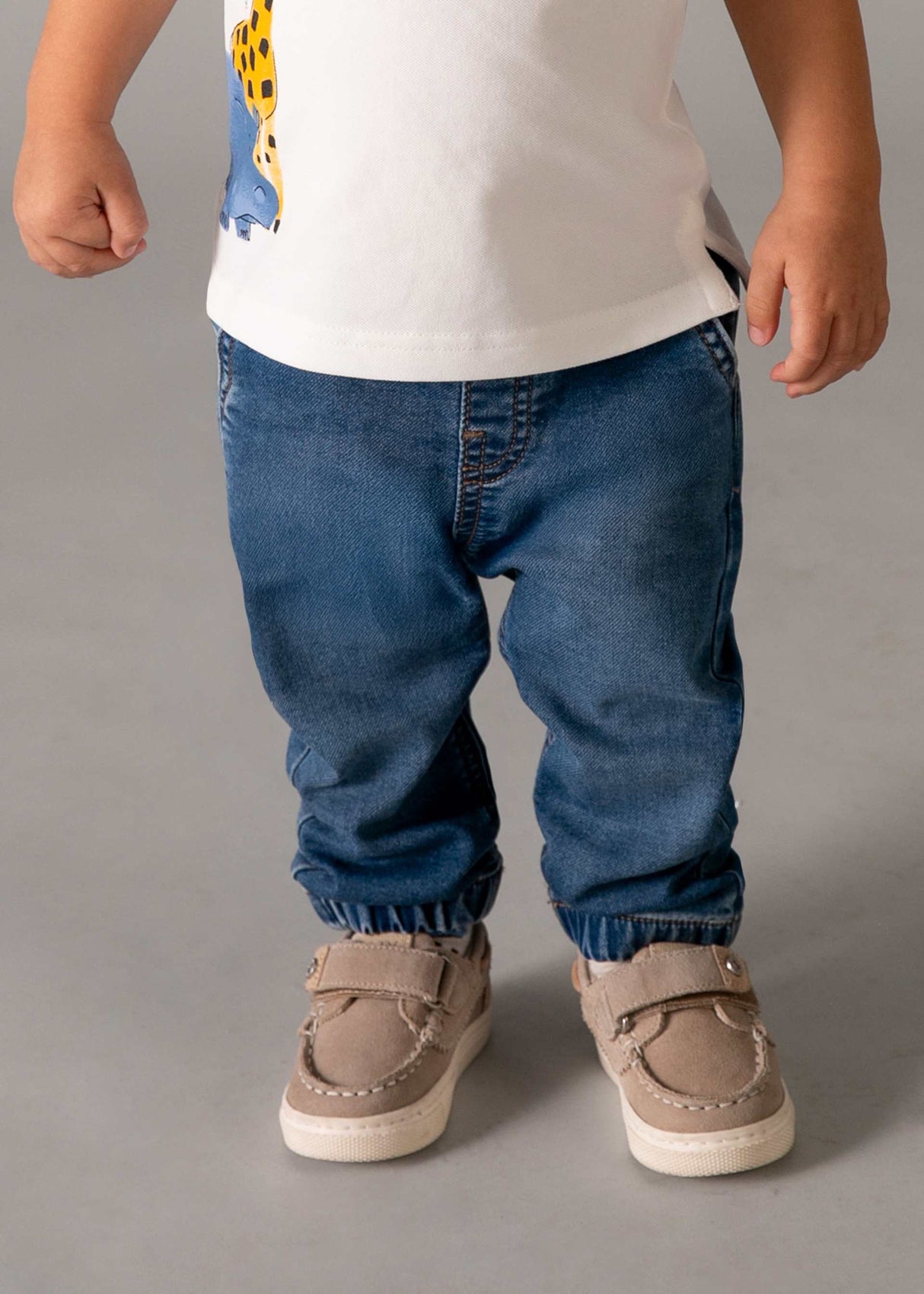 Closeup lifestyle view of baby boy elastic waist jeans styled with a white tee.