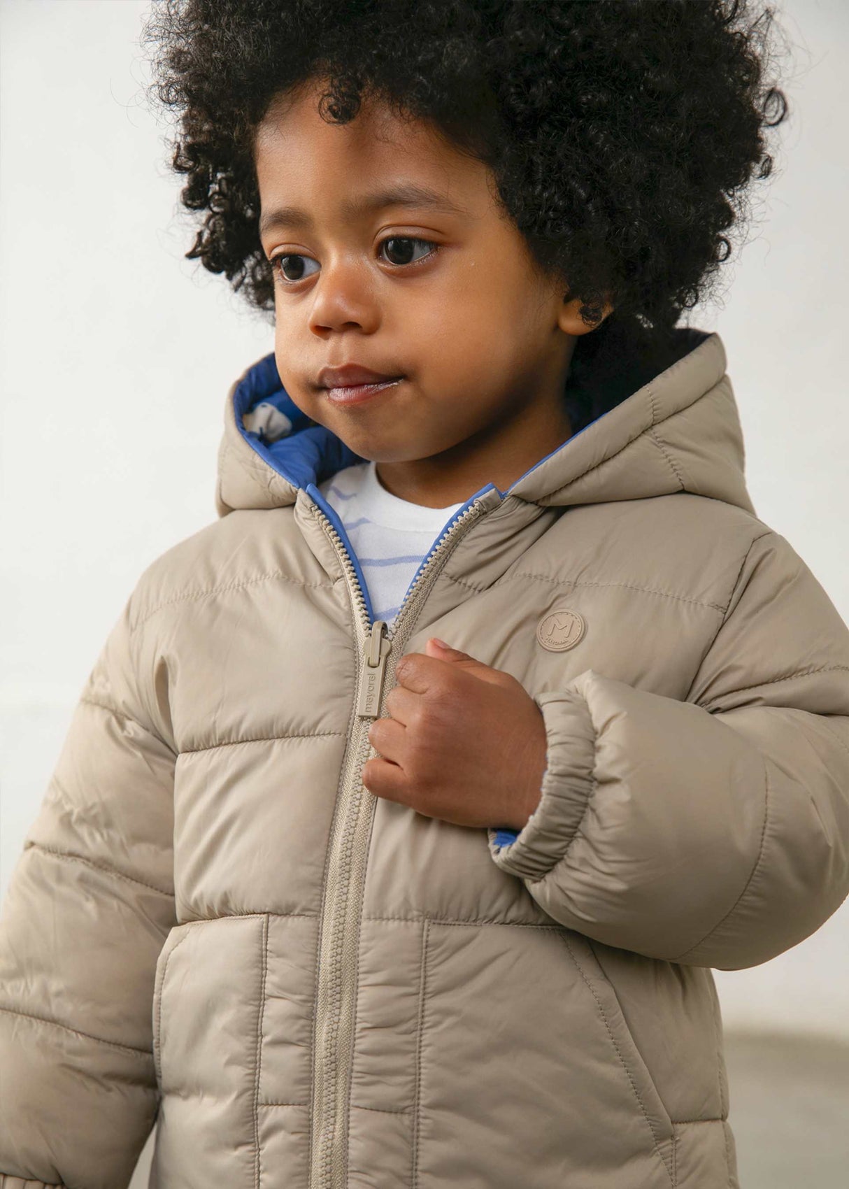 Baby boy wearing Mayoral reversible puffer jacket on the solid Taupe side for neutral winter styling.