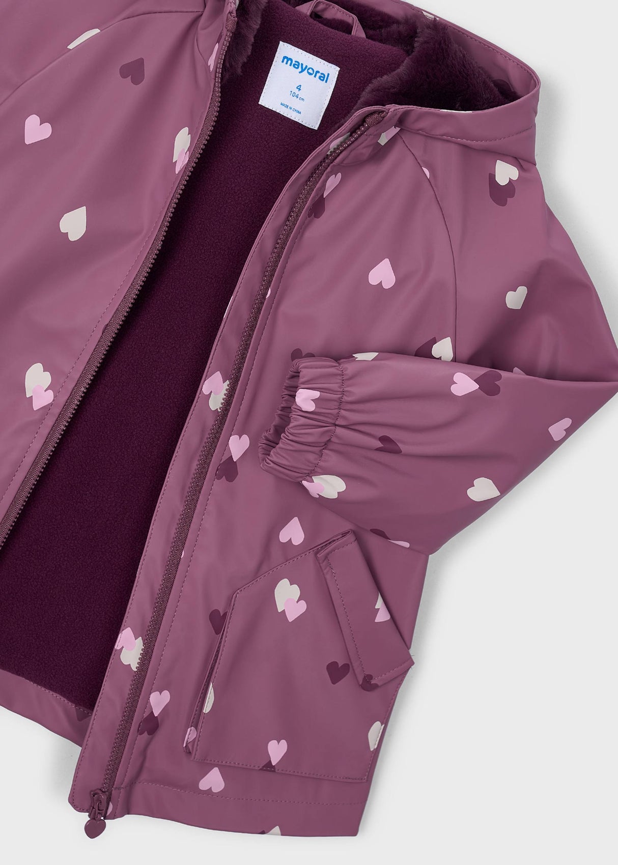 Close-up of Mayoral girls raincoat showing zip front, soft lining, hood, and heart print detail.