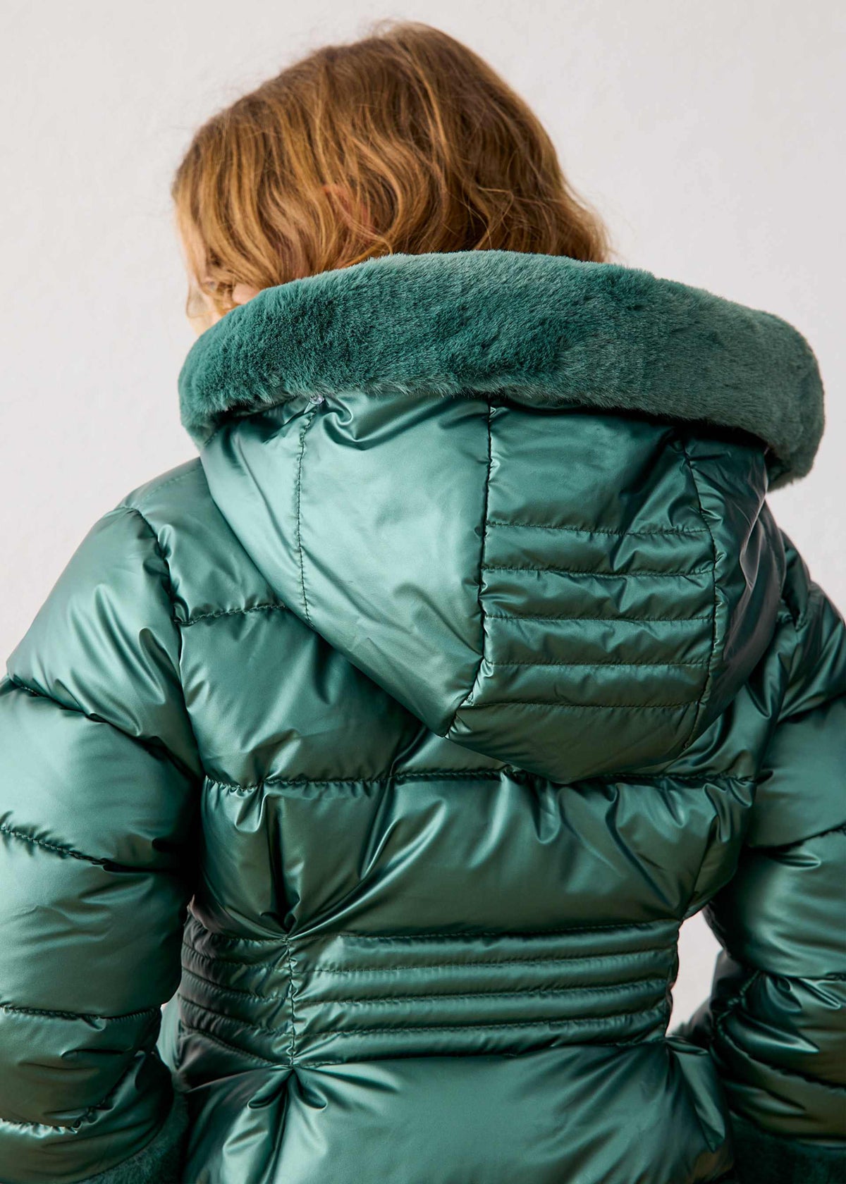 Child seen from behind in the metallic green quilted puffer jacket with a faux fur hood collar