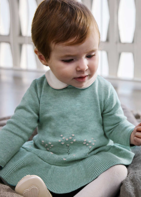 Baby wearing the sage green knit dress with a white collar and ribbed ruffle hem